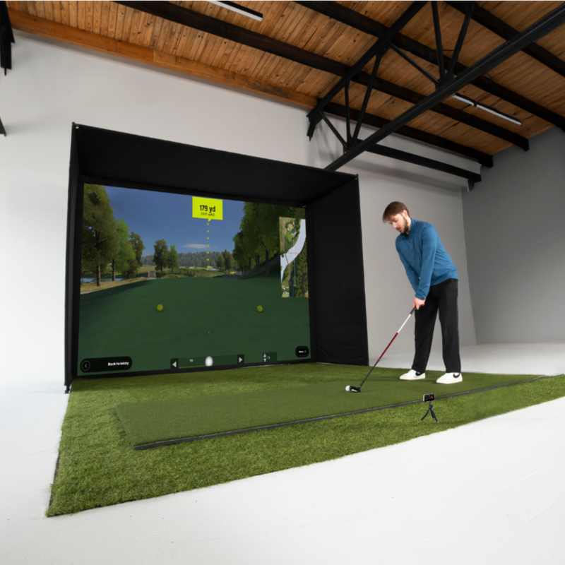 Person practicing golf indoors using a screen and mobile simulator displaying a virtual golf course.