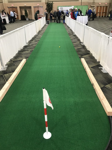 Green indoor putting green with a white flag at a convention center.