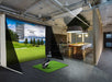 Golf simulator setup in a modern indoor space with a large screen displaying a golf course.