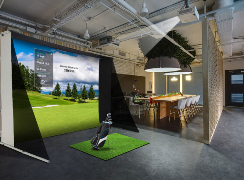 Golf simulator setup in a modern indoor space with a large screen displaying a golf course.