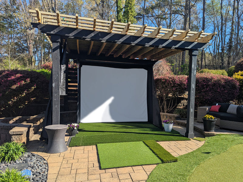 Outdoor setup with a portable screen, grass, and a pergola in a garden.