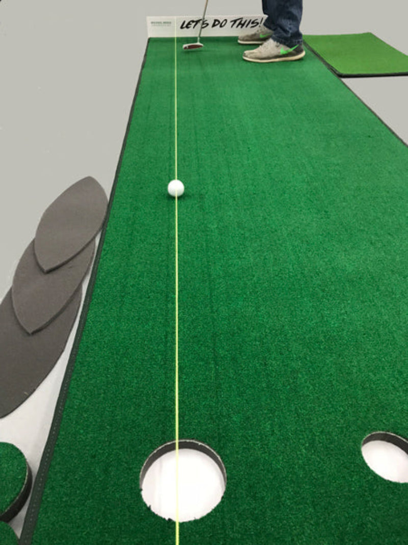 Putting green setup with a green mat, white ball, and hole on a gray floor.
