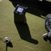 Golf ball on a tee with TruGolf Launch Box device and basket of golf balls on a green surface