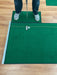 Person practicing golf on a green mat with a wooden floor background