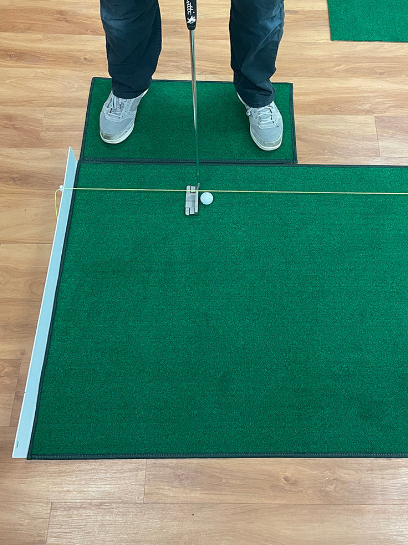 Person practicing golf on a green mat with a wooden floor background