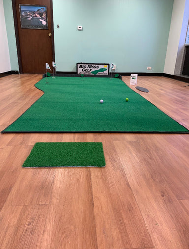 Indoor golf practice area with green mat and golf balls on wooden floor.