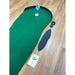 Putting green setup on a wooden floor with a green mat, white ball, and accessories.
